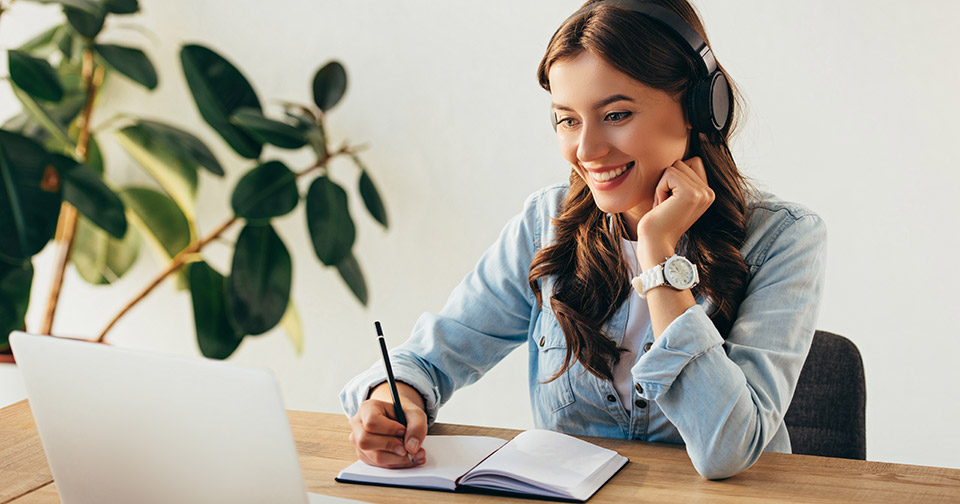 image of a woman taking notes while listening to something on her laptop